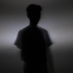 Silhouette of a person standing in a beam of light. Their features are not visible.